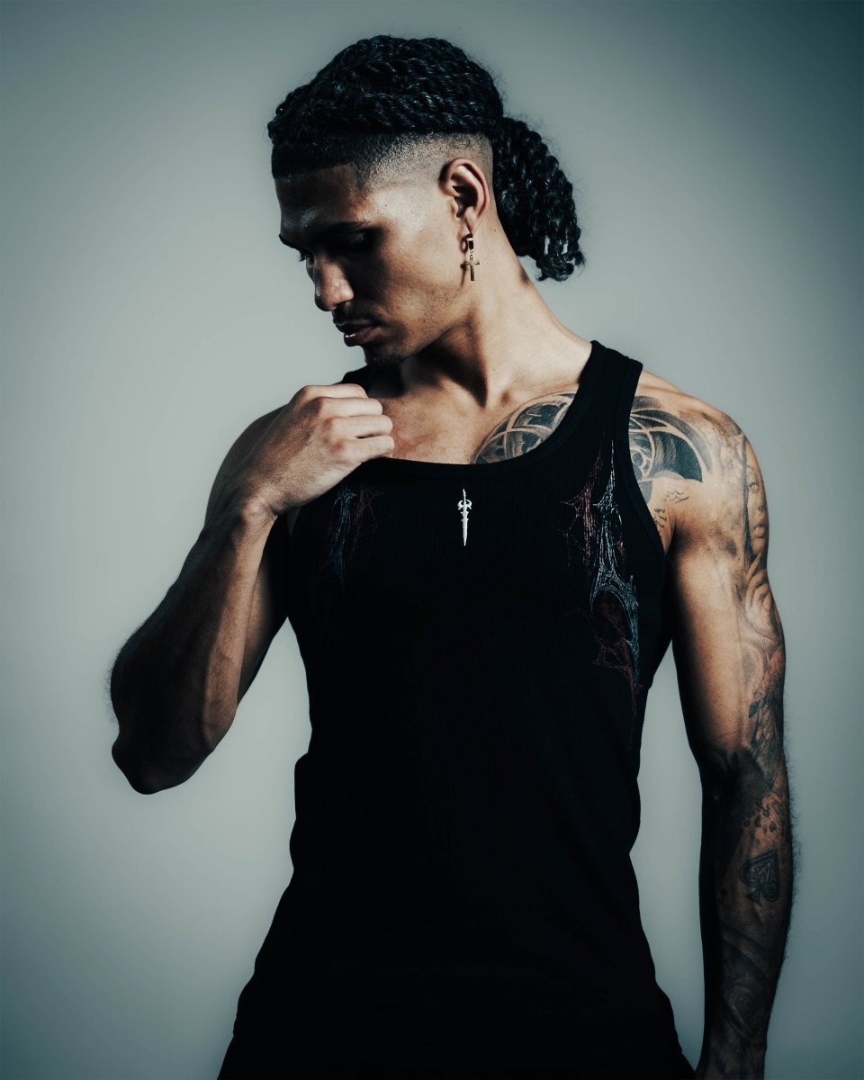 Man wearing a black tank top with tattoos on his arms against a gray background