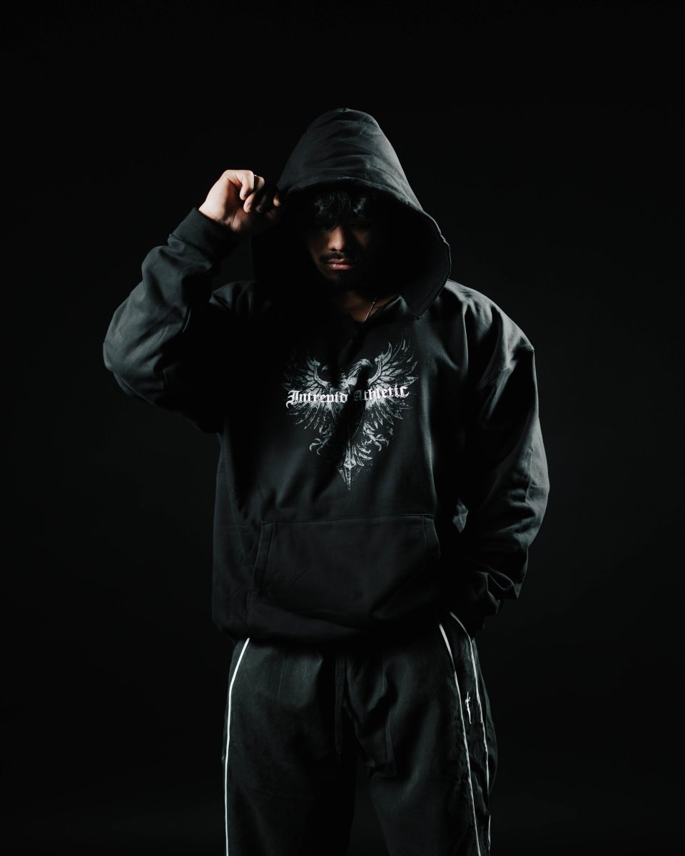 Person wearing a black hoodie with a logo on a dark background
