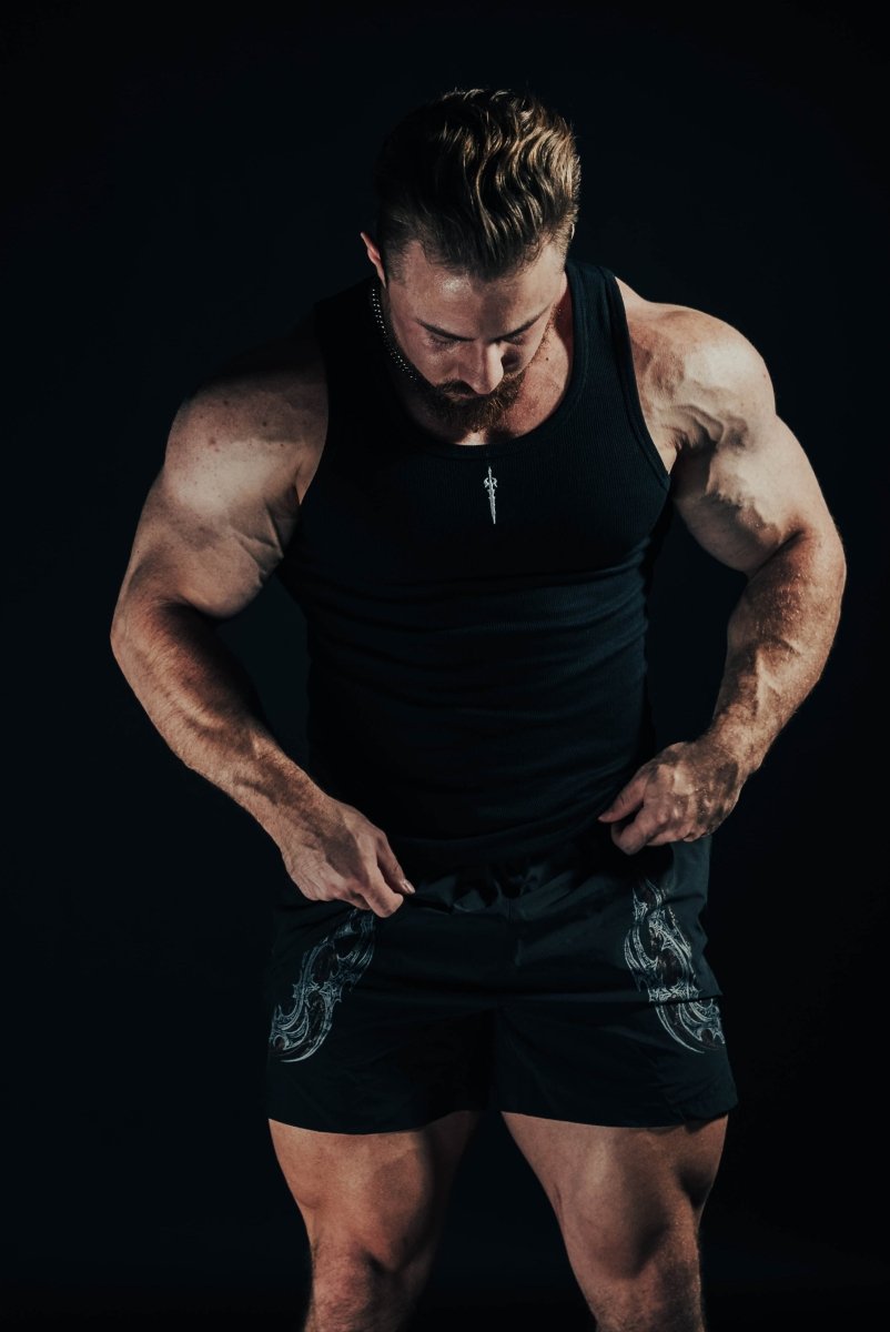 Muscular man wearing a black tank top and shorts on a dark background