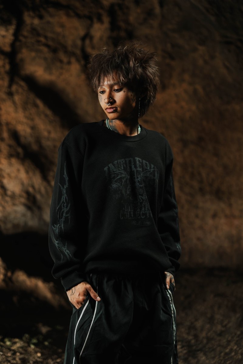 Person wearing a black sweatshirt with text, standing against a textured brown wall.