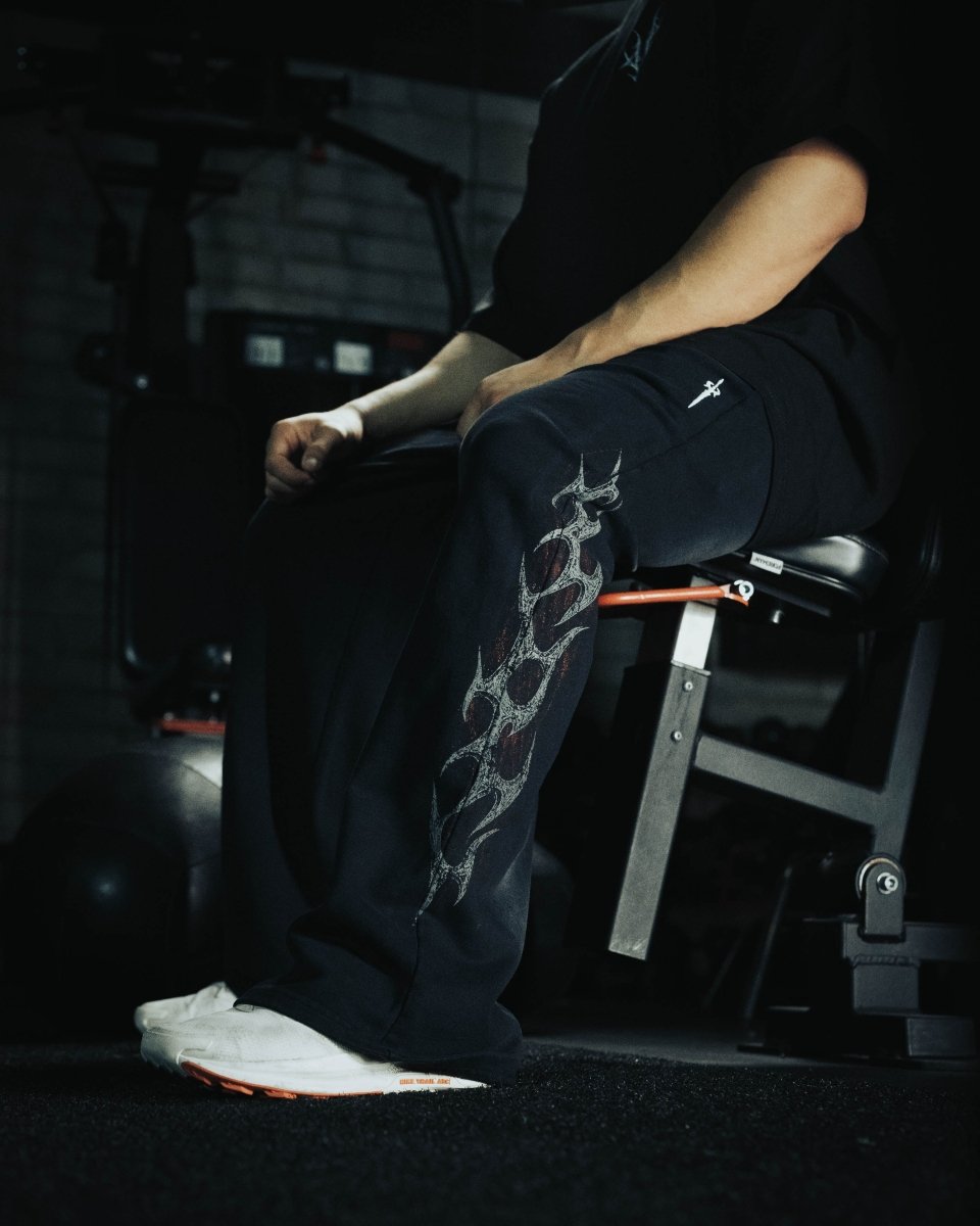Person sitting on a weight bench in a gym setting with tattoos visible on their legs.