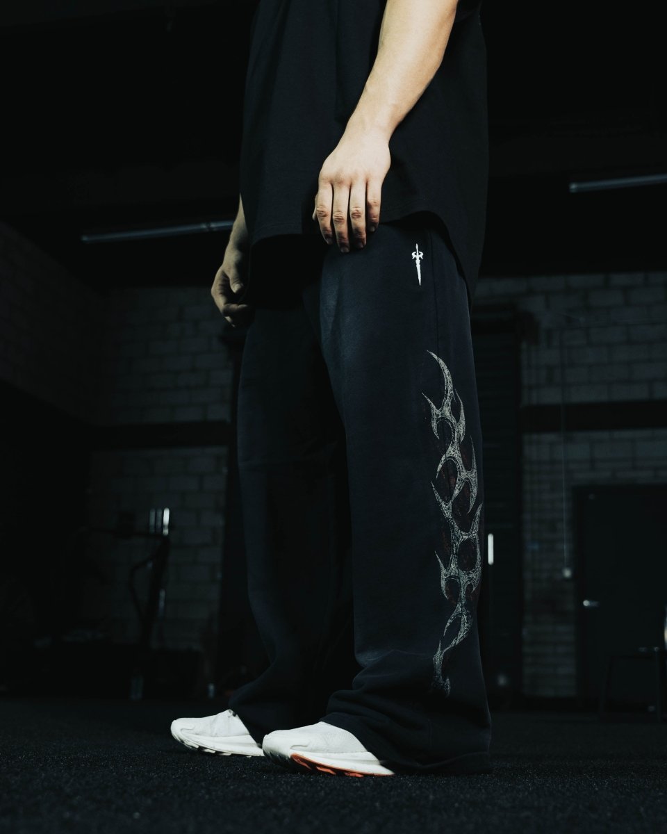 Person wearing black pants with a white design and white shoes in a dark setting