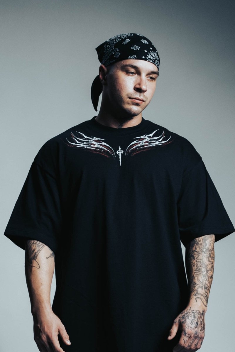 Man wearing a black t-shirt with white designs and a bandana, standing against a gray background
