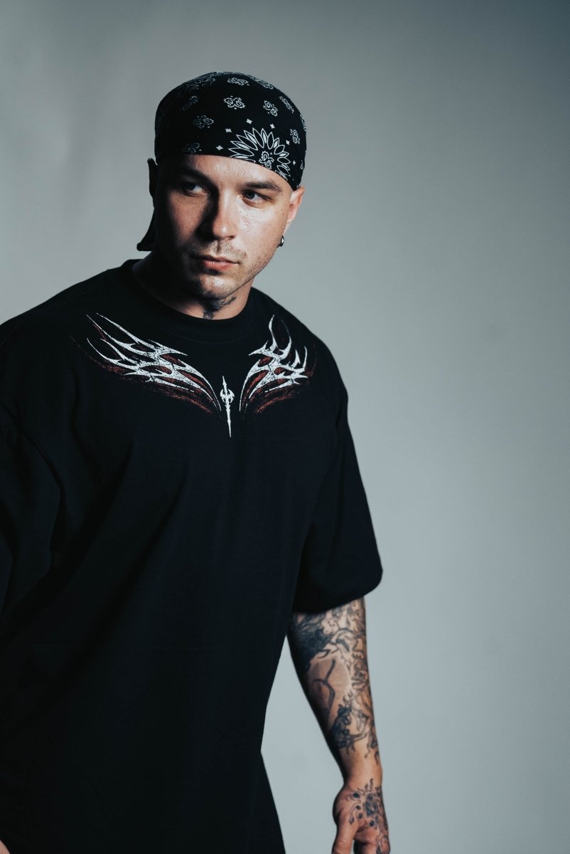 Man wearing a black t-shirt with a white design and a bandana, standing against a gray background