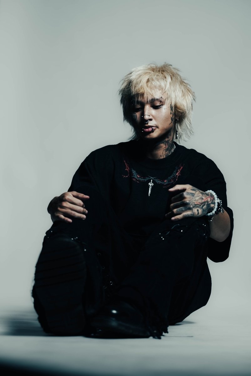 Person with tattoos wearing a black outfit against a gray background