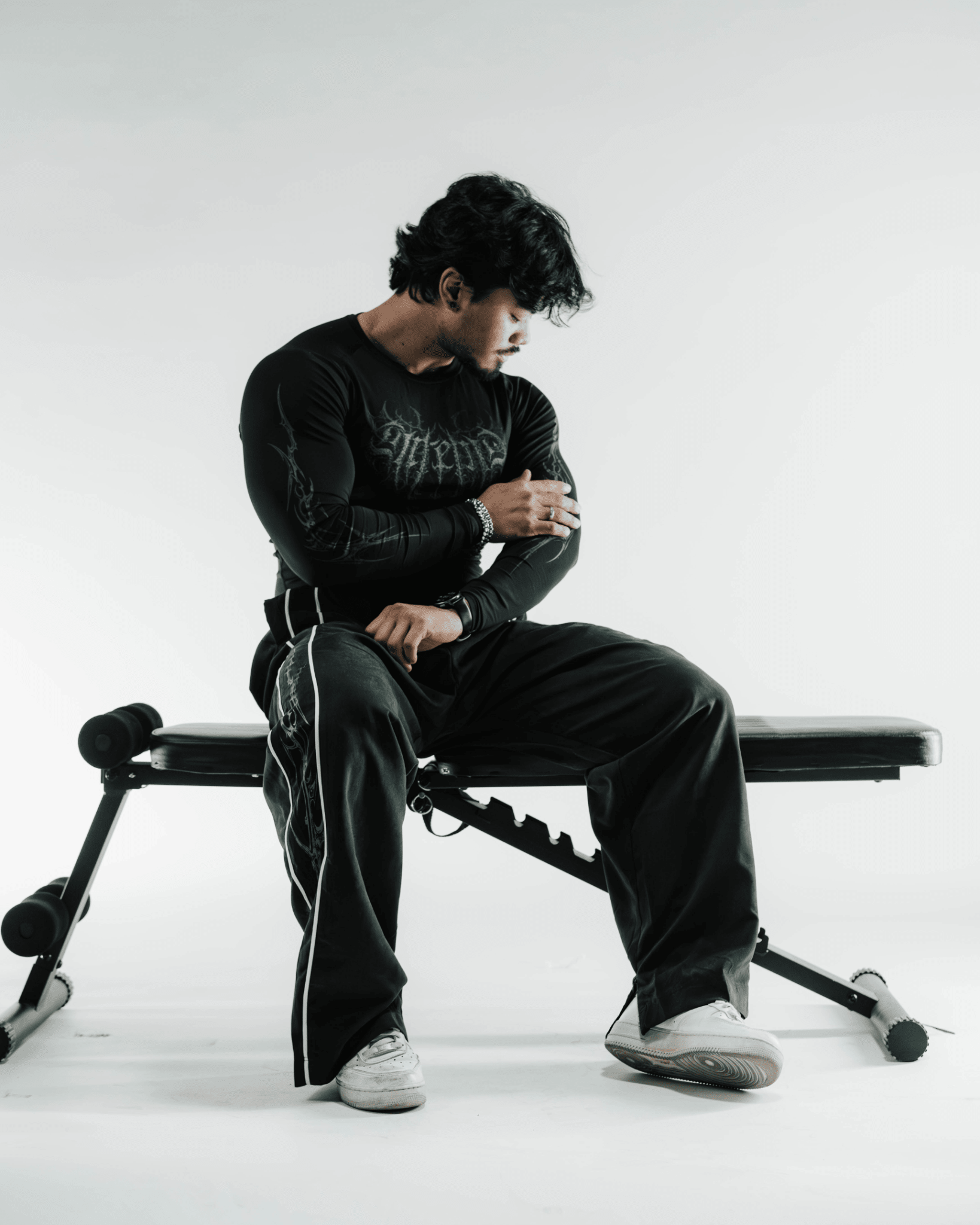 Person sitting on a weight bench wearing a black outfit with a white background