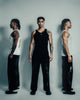 Three men wearing tank tops and pants against a plain background