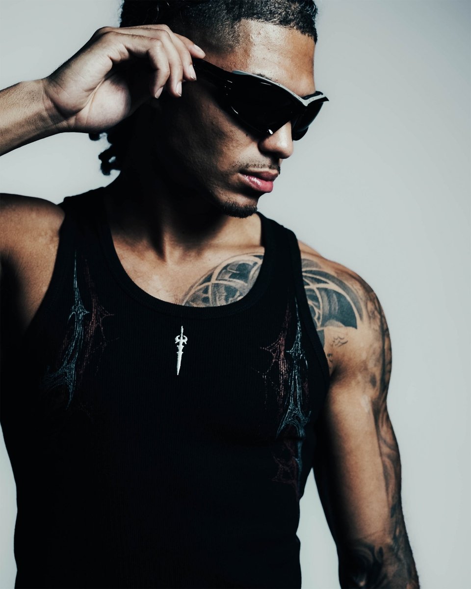 Man wearing a black tank top with tattoos on his arms against a plain background