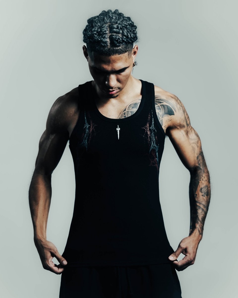 Man wearing a black tank top with tattoos on a gray background