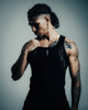 Man wearing a black tank top with tattoos on his arms against a gray background