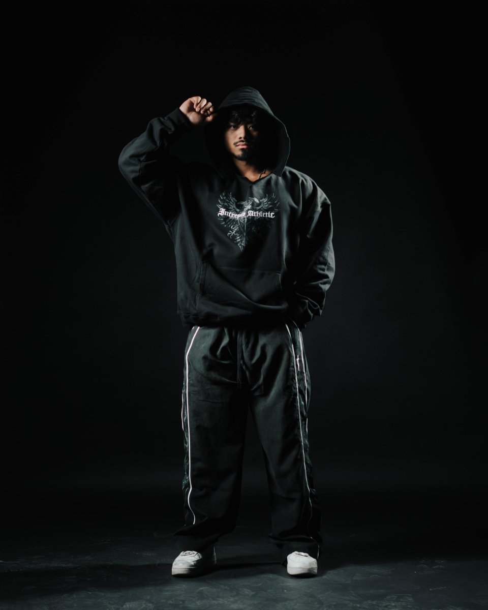 Person wearing a black hoodie and pants with a logo on a dark background