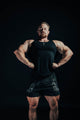 Muscular man posing in black tank top and shorts against a dark background