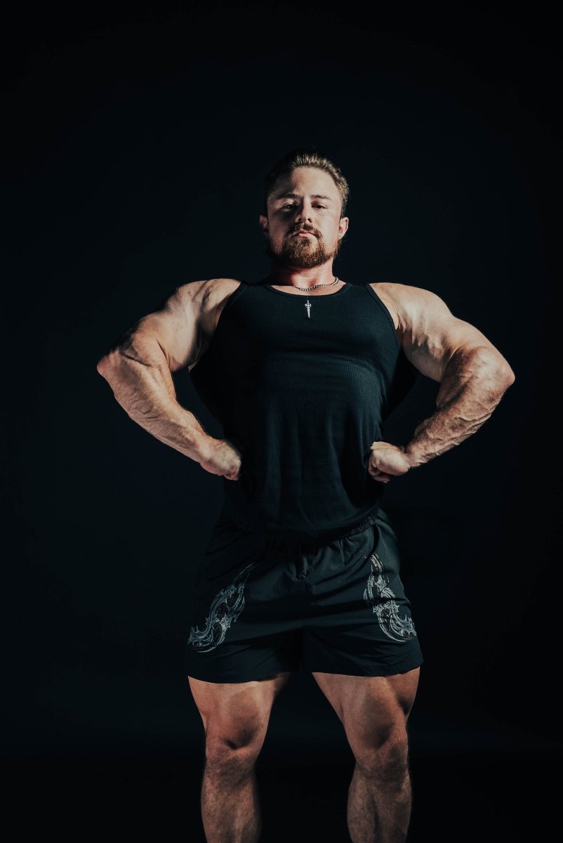 Muscular man posing in black tank top and shorts against a dark background