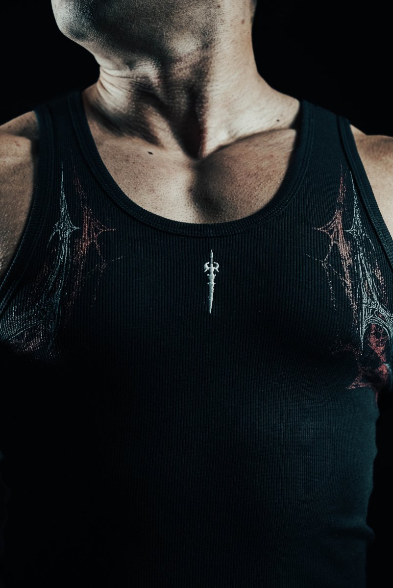 Person wearing a black tank top with intricate designs on a dark background