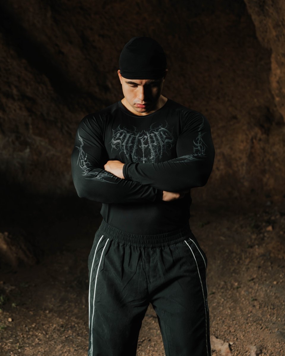 Person wearing a black long-sleeve shirt with graphic design and black pants in a dark cave setting