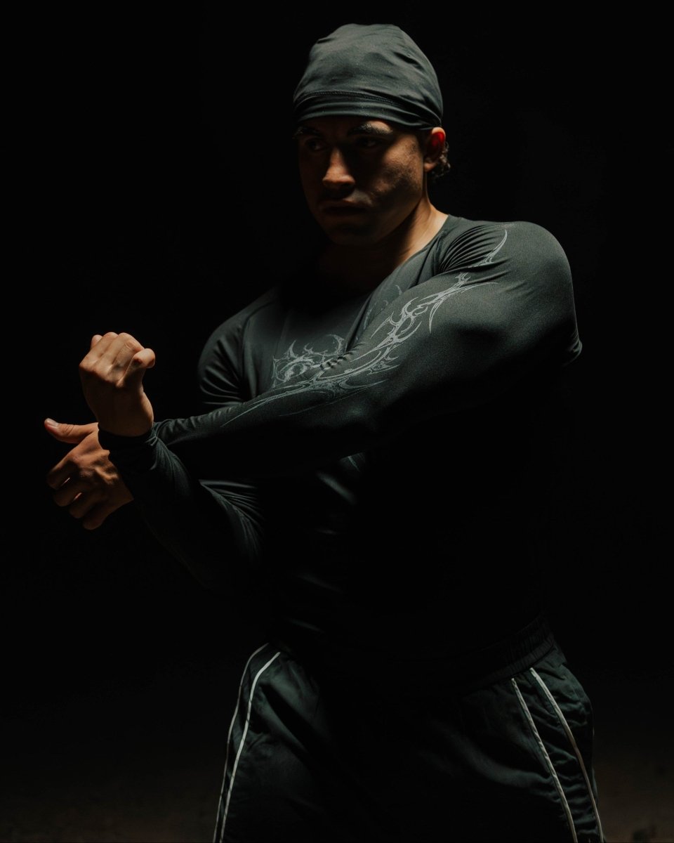 Person in dark clothing with a head covering in a dramatic pose against a black background