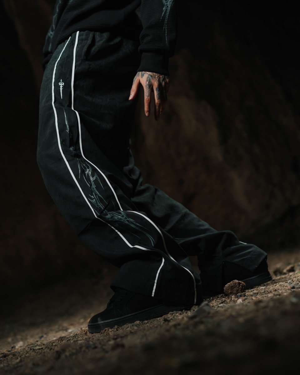 Person wearing black pants with white stripes sitting on the ground in a dark setting