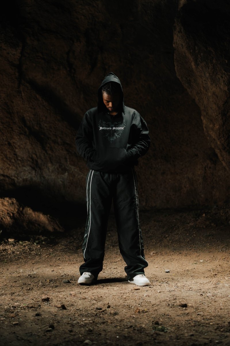 Person wearing a dark hoodie and pants standing in a dark, rocky area.