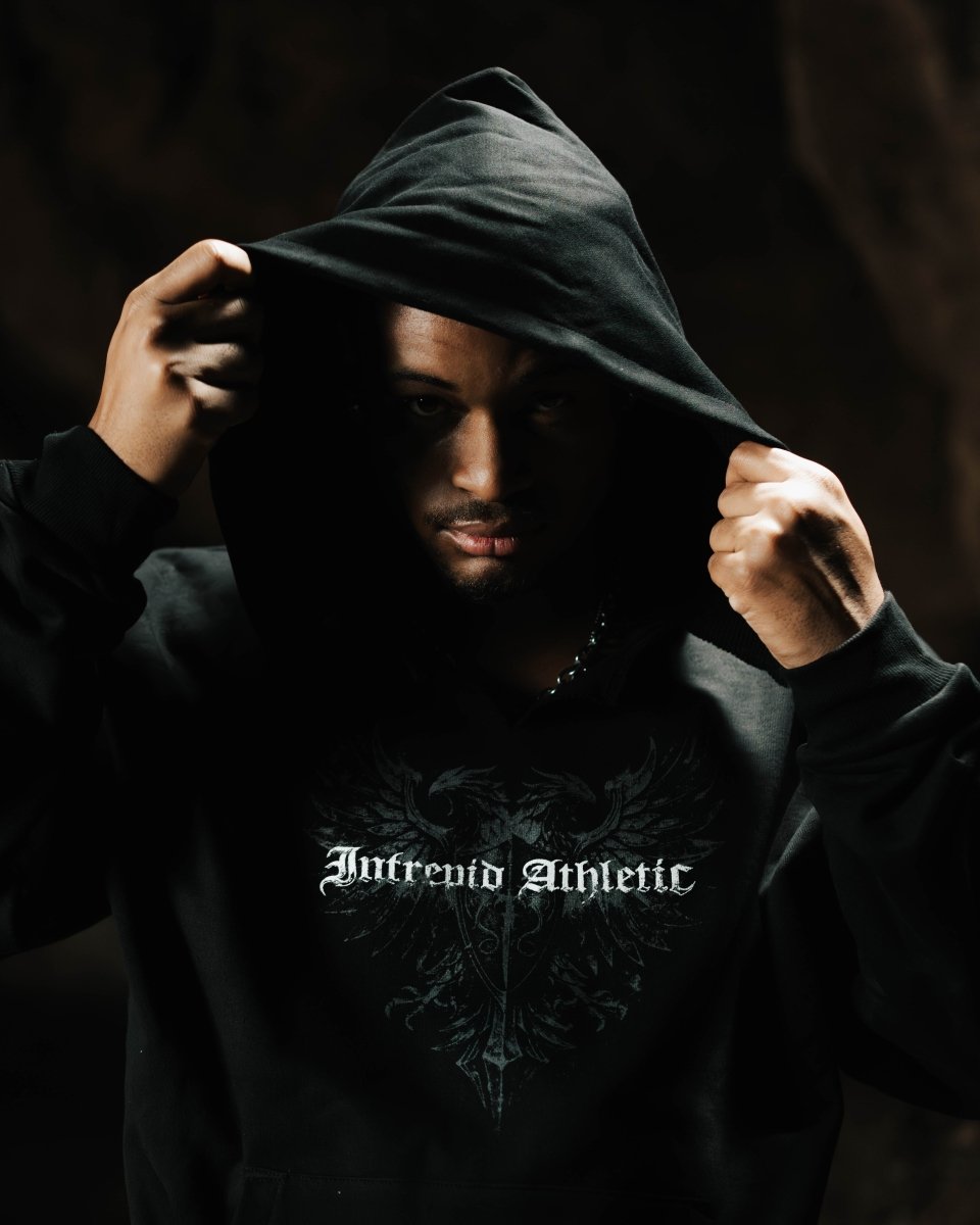 Person wearing a black hoodie with 'Intrepid Athletic' text, holding the hood over their head.