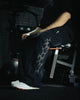 Person sitting on a weight bench in a gym setting with tattoos visible on their legs.