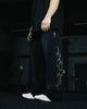 Person wearing black pants with a white design and white shoes in a dark setting