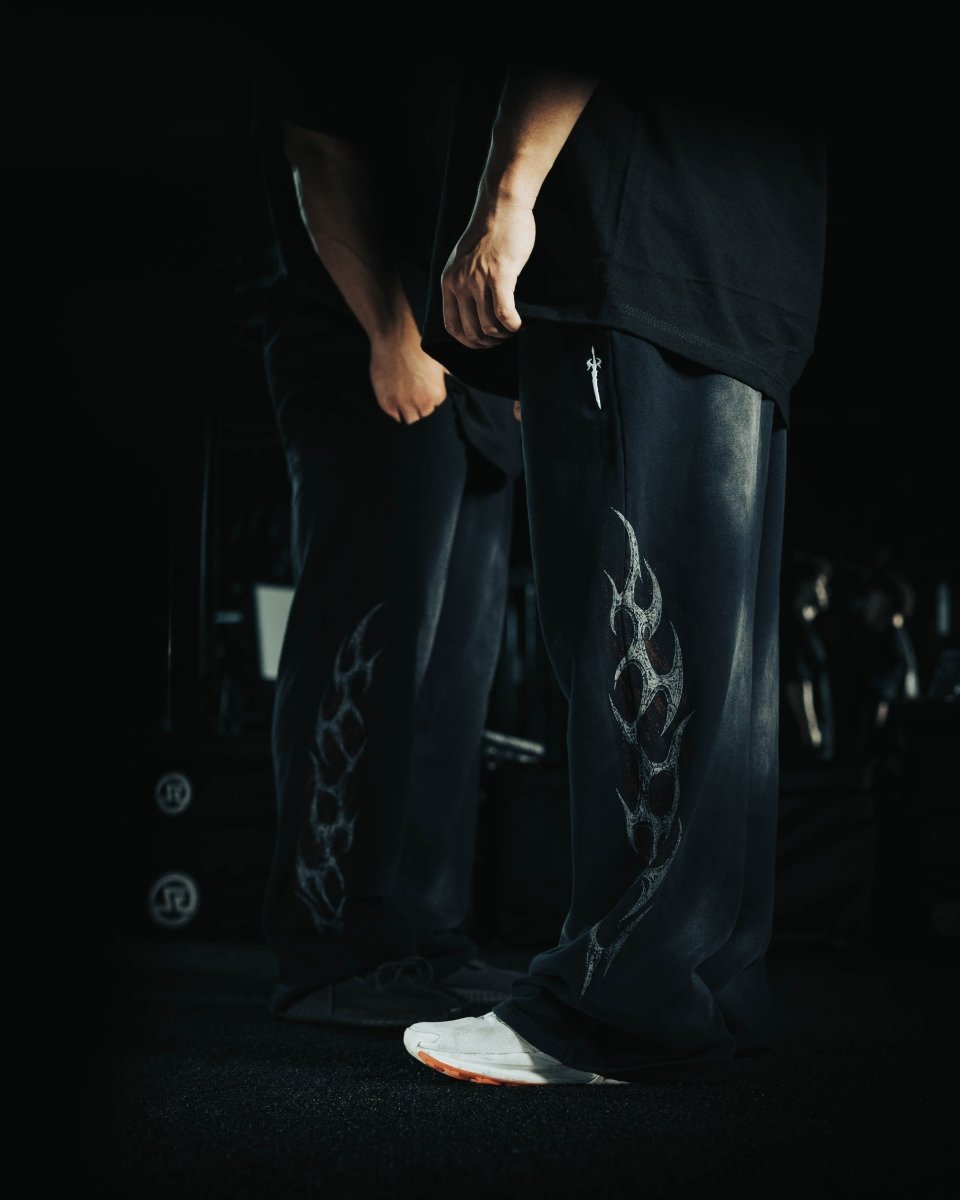 Person wearing dark pants with a flame design in a dimly lit setting