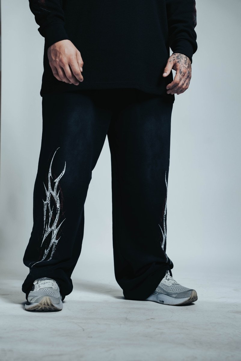 Person wearing black pants with white design and gray sneakers on a light background