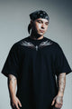 Man wearing a black t-shirt with white designs and a bandana, standing against a gray background