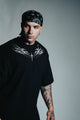 Man wearing a black t-shirt with a white design and a bandana, standing against a gray background