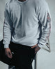 Person wearing a light gray sweatshirt with floral patterns on sleeves, sitting on a stool.