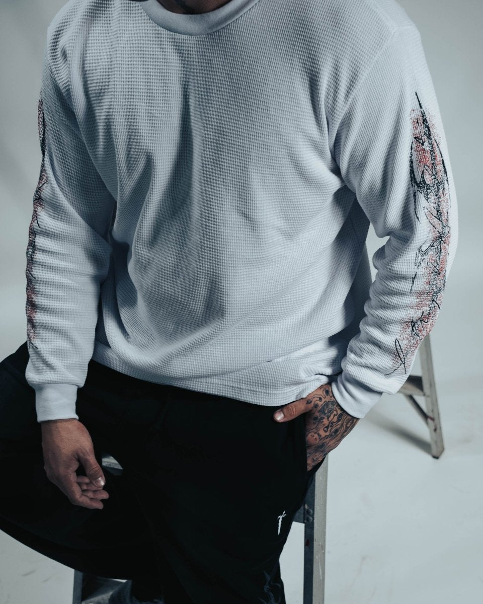 Person wearing a light gray sweatshirt with floral patterns on sleeves, sitting on a stool.