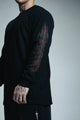 Person wearing a black long-sleeve shirt with a detailed design on the sleeve against a gray background