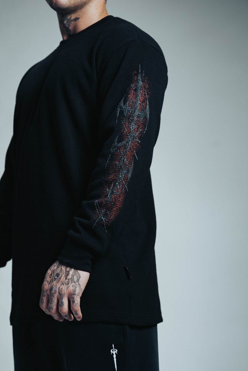 Person wearing a black long-sleeve shirt with a detailed design on the sleeve against a gray background