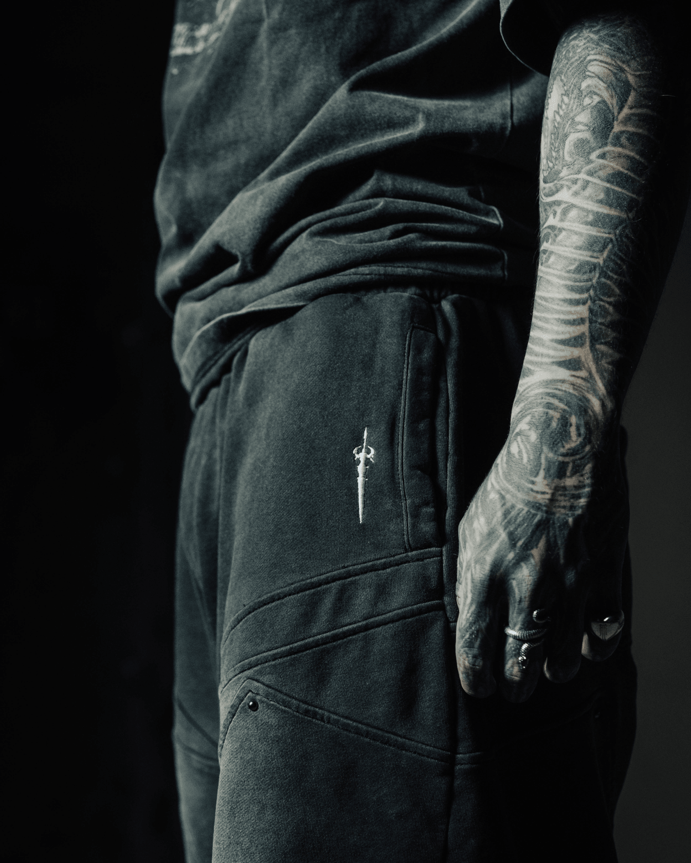 Person wearing black pants with a visible brand logo, standing against a dark background.