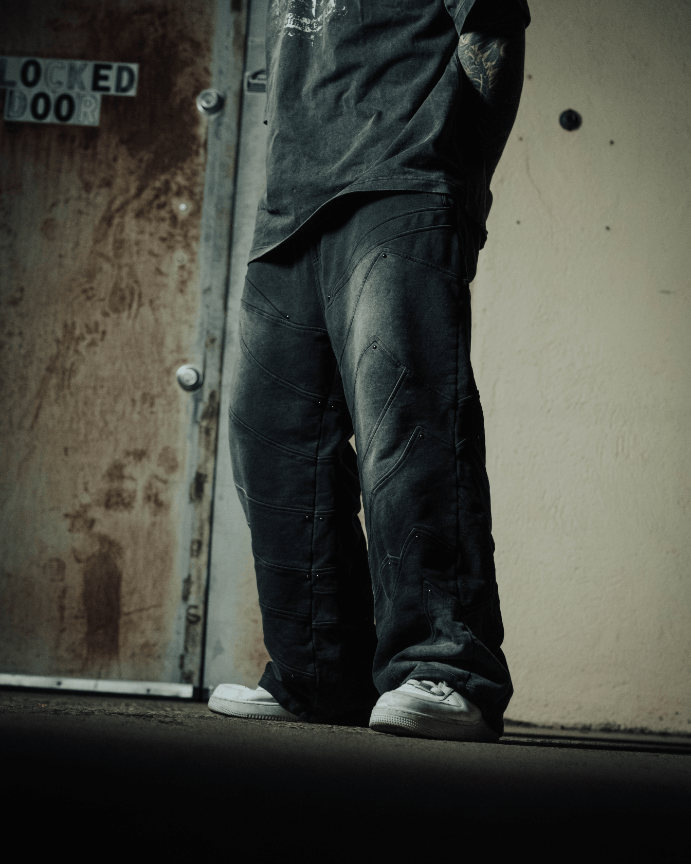 Person wearing dark pants and white shoes standing against a textured wall.
