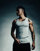 Man wearing a gray tank top with tattoos on his arms against a dark background