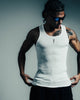 Man wearing a white tank top with tattoos on a gray background