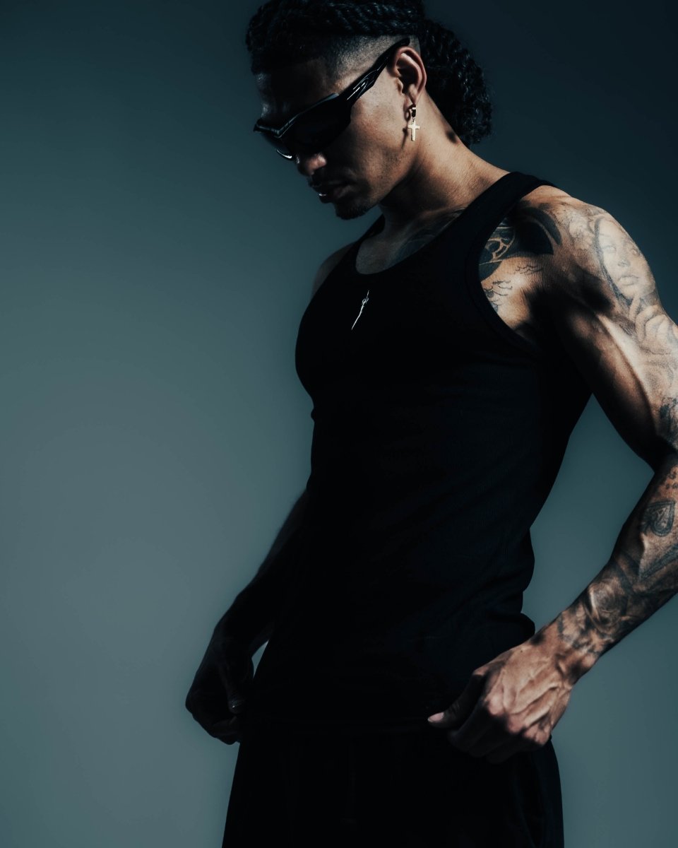 Person wearing a black tank top with tattoos on arms against a dark background