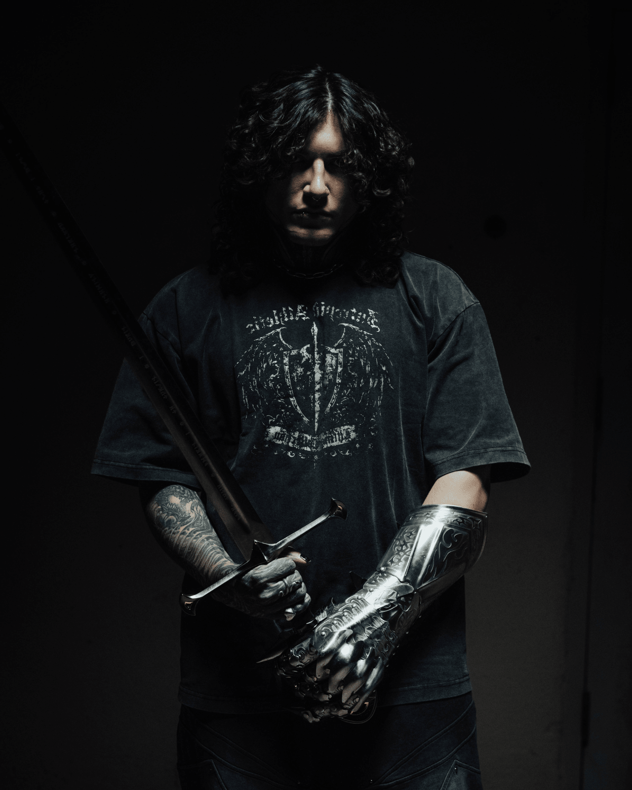 Person wearing a dark t-shirt with visible text and metallic arm prosthetic against a black background