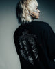 Person wearing a black jacket with intricate designs on the back against a gray background