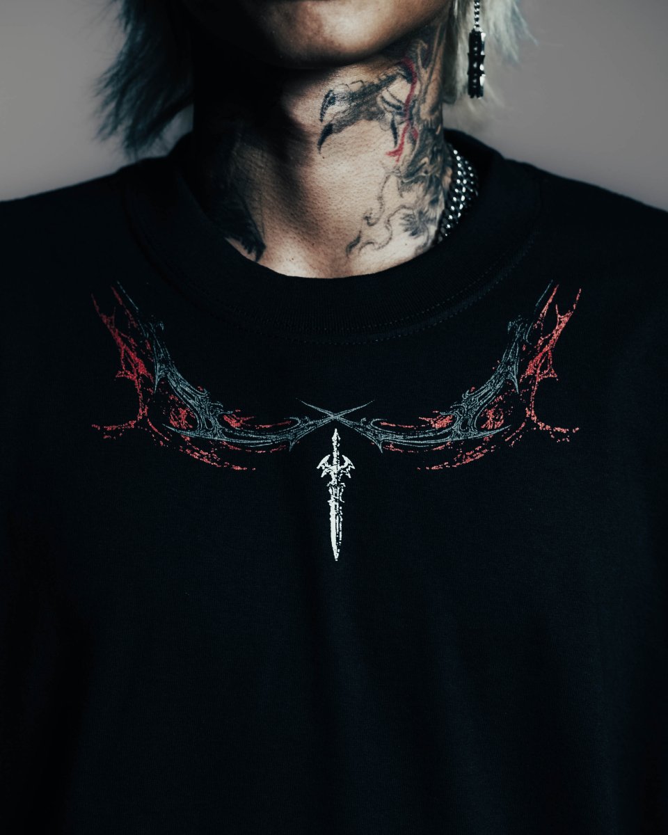 Person wearing a black shirt with a necklace design and tattoos on neck