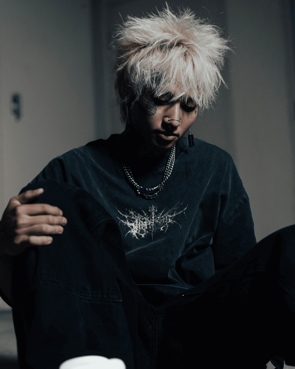 Person wearing a dark hoodie with a logo, sitting indoors.